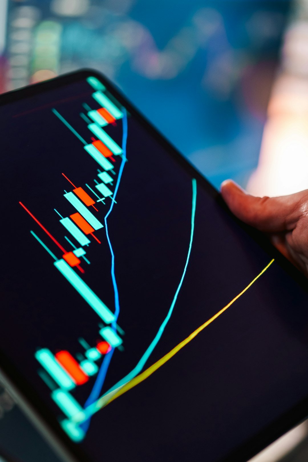 Hand holding a tablet showing a stock market candlestick chart in a trading app