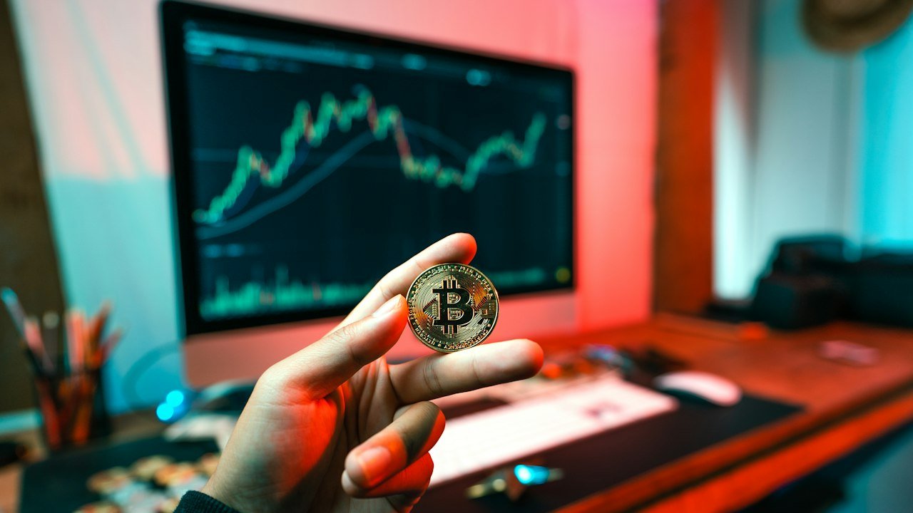 Person holding a coin in front of a computer, researching cryptocurrencies under $1